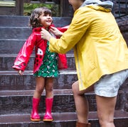 parent in yellow rain jacket putting ladybug rain coat on young child