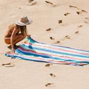 woman in straw hat laying down oversized striped towel on beach